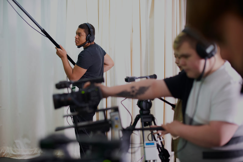 Boom operator in headphones holding a microphone pole beside a camera crew.