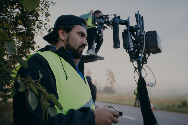 Crew member with a wireless handset beside a cinema camera on a crane at dawn.